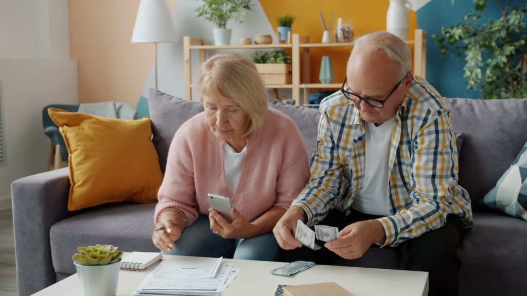 healthy-woman-legs-dark Elderly couple budgeting at home, seated on a cozy sofa, using smartphone and cash.